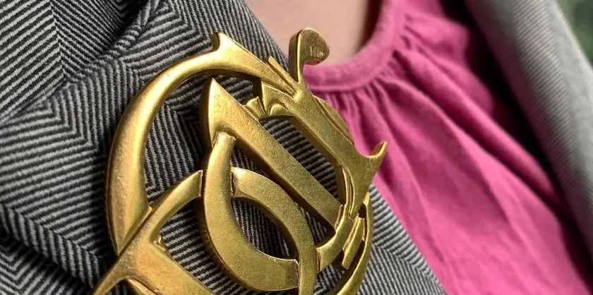 Gold tone Christian Dior logo brooch on grey blazer