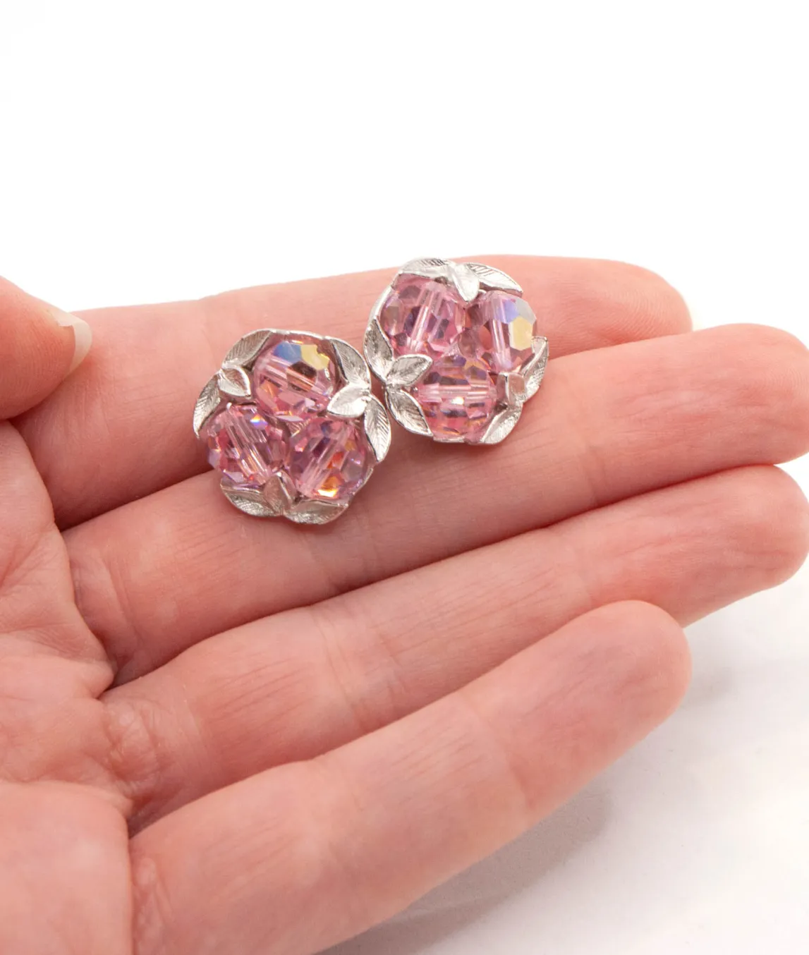 Small pink vintage earrings in silver metal held in a hand