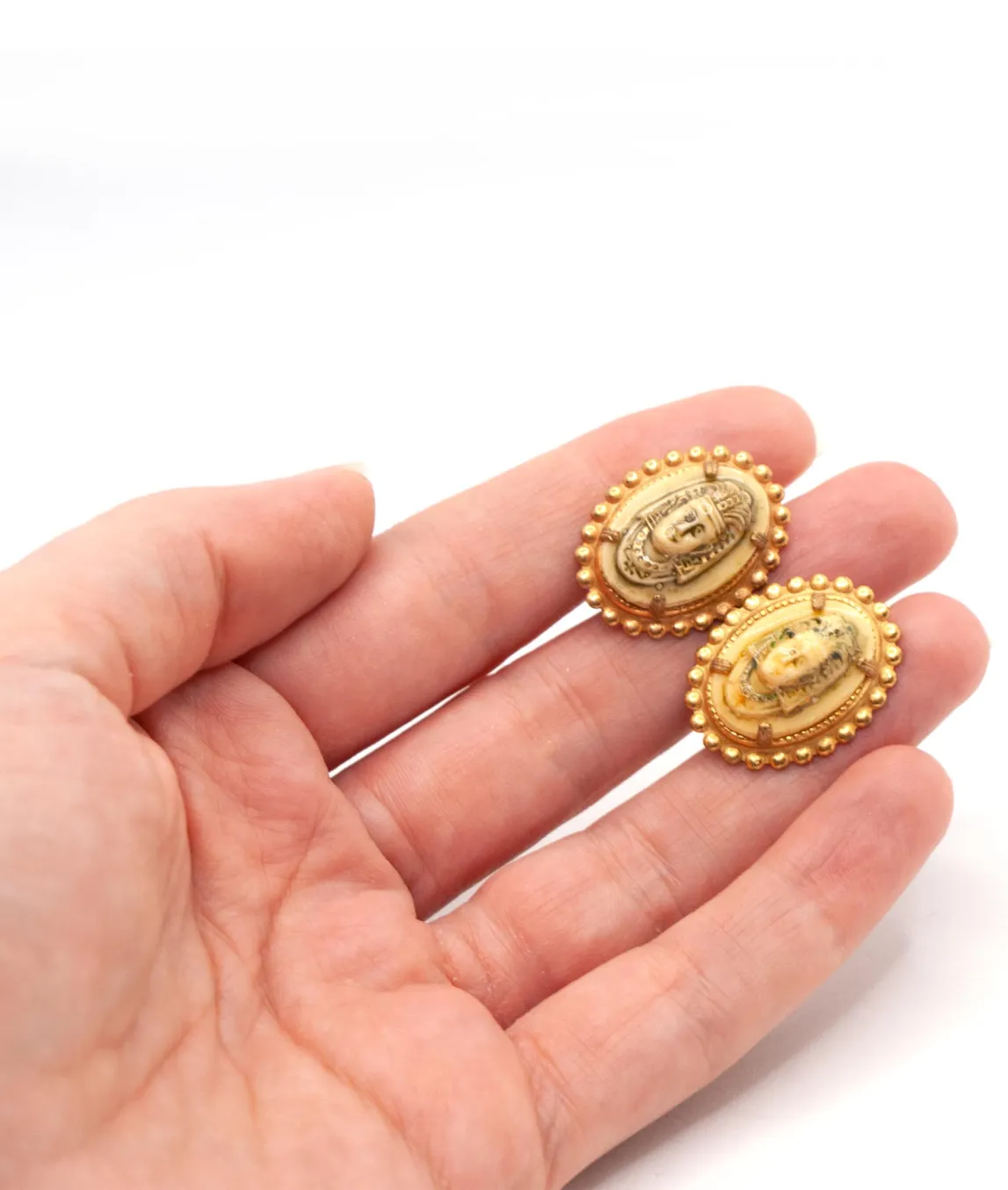 Miriam Haskell cream and golden Egyptian earrings held in a hand