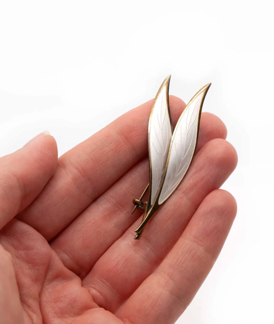 Double leaf brooch by NM Thune of Norway white enamel with gold edges held in hand