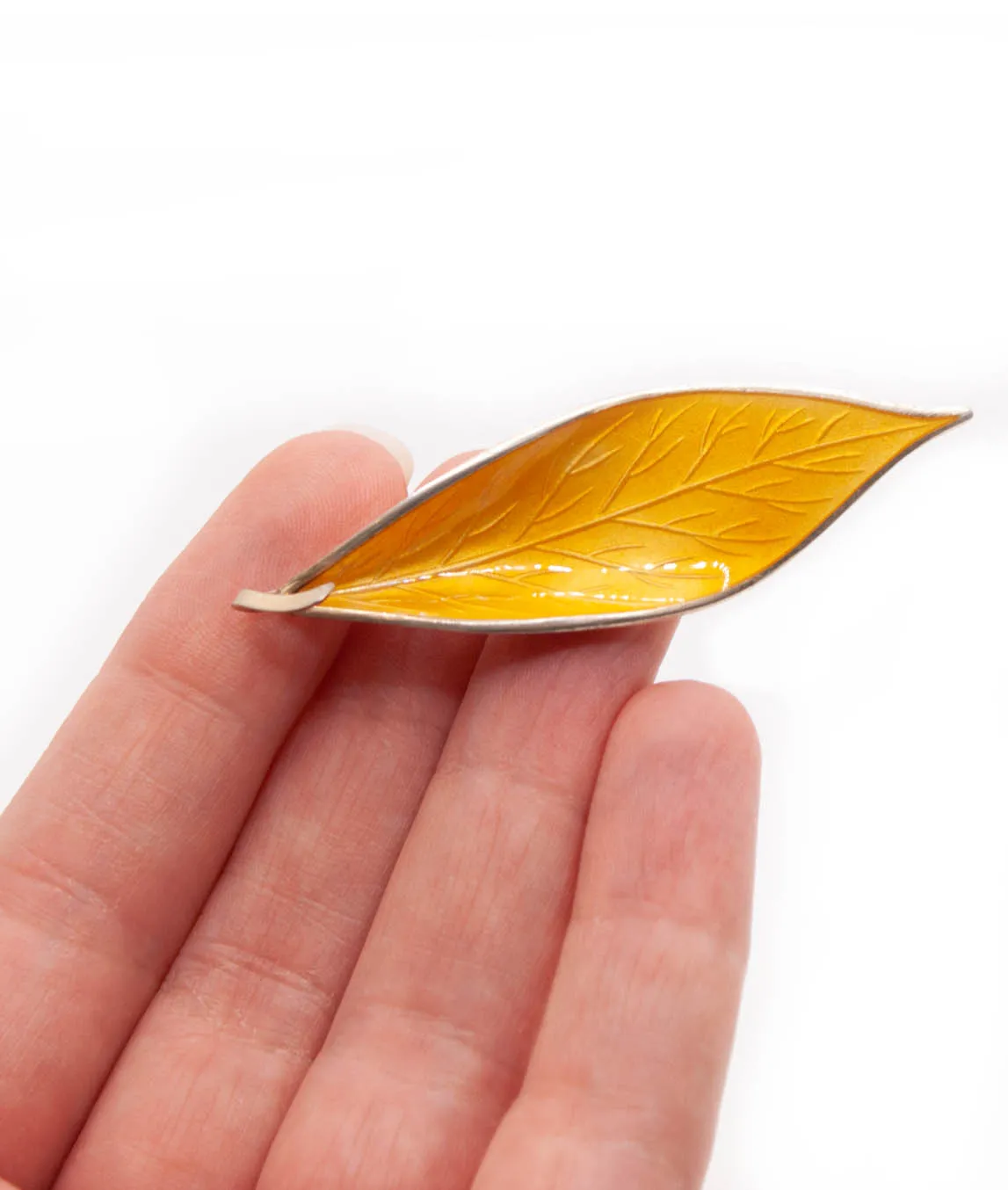 Yellow enamel on silver leaf brooch by David Andersen held in a hand
