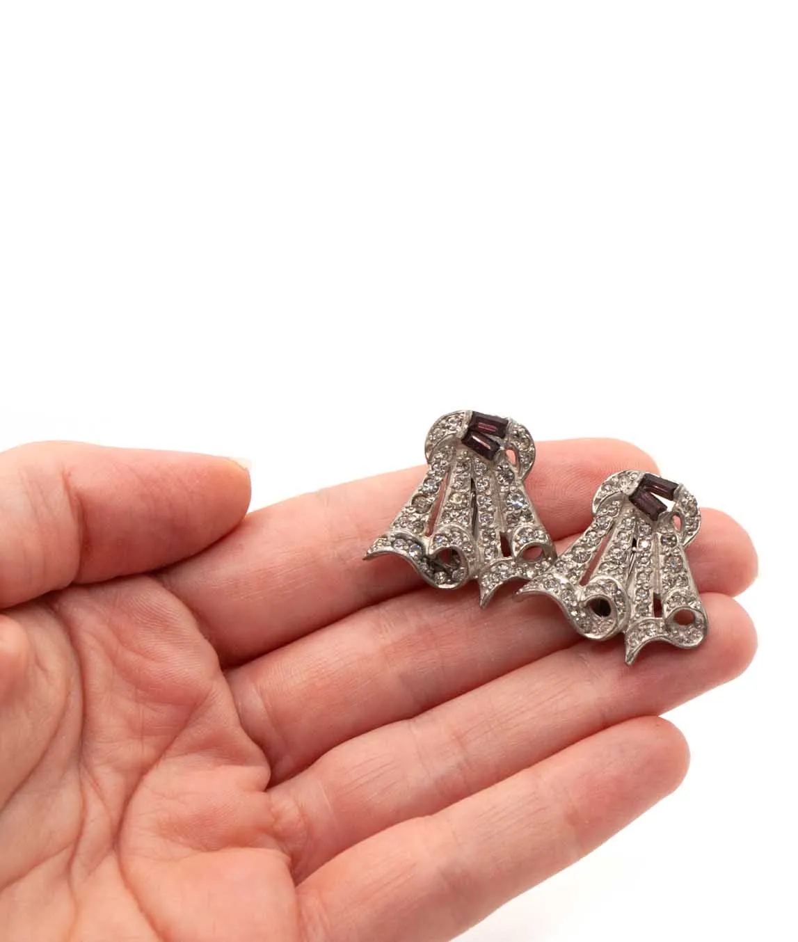 Two Art Deco dress clips held in a hand under studio lighting