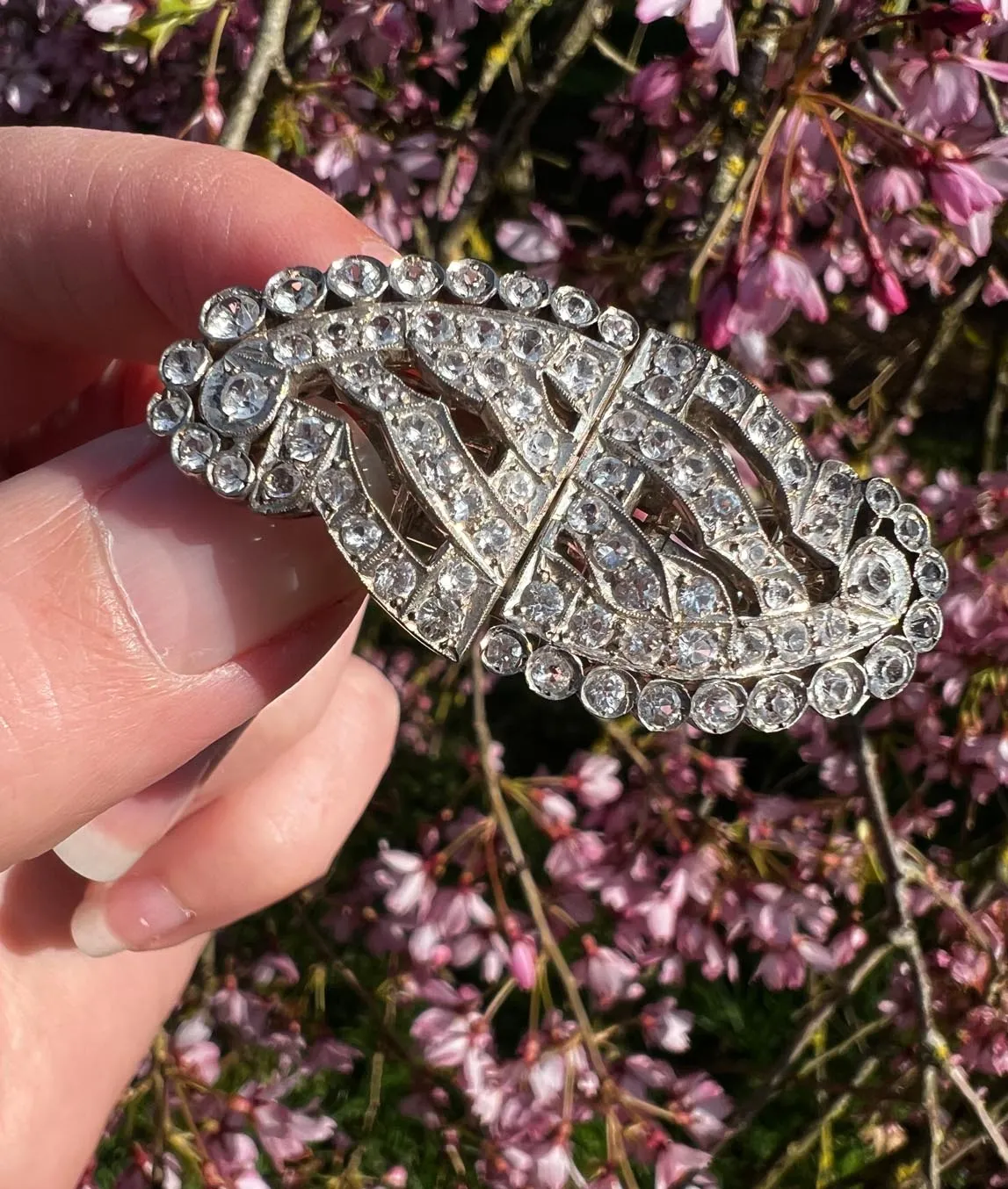 Art Deco dress clips as brooch held in hand in front of pink flowers