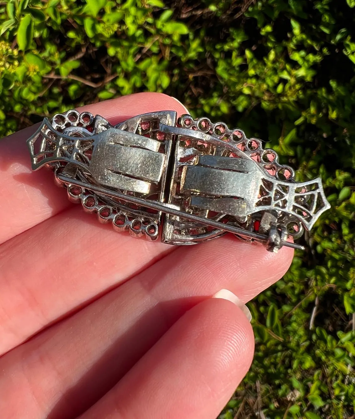 Back of Indian silver double dress clip brooch held in a hand in front of greenery