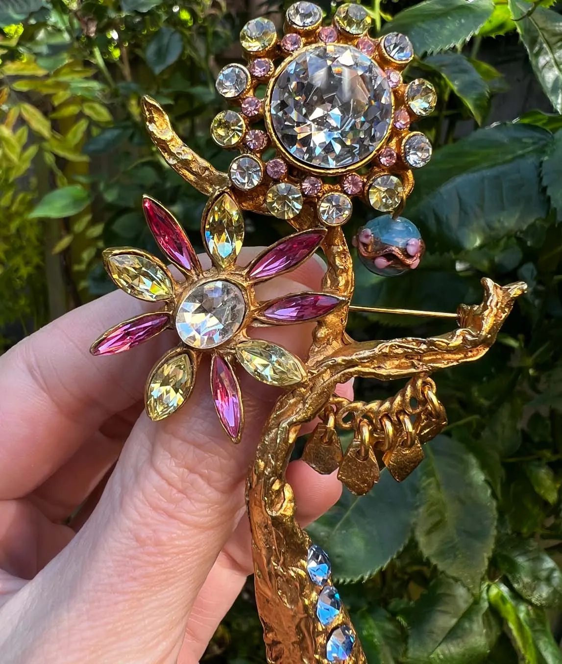 Large Christian Lacroix golden flower brooch with pink and green rhinestone flowers held over greenery
