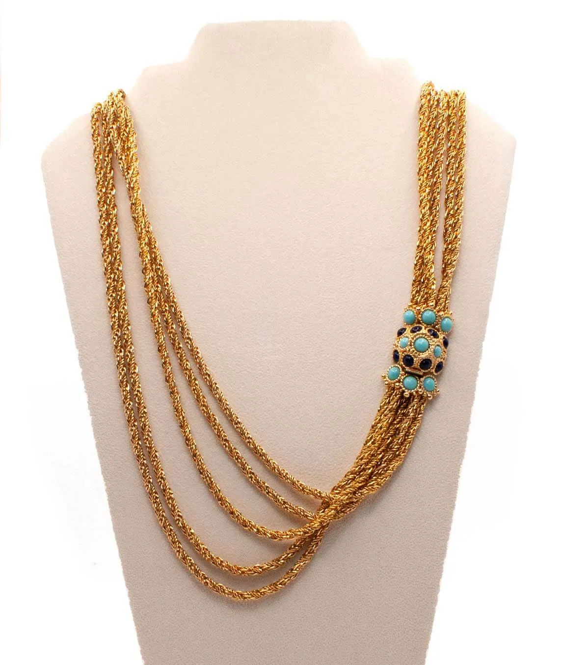 Christian Dior chain necklace with turquoise and blue glass decorative clasp on a beige velvet display stand