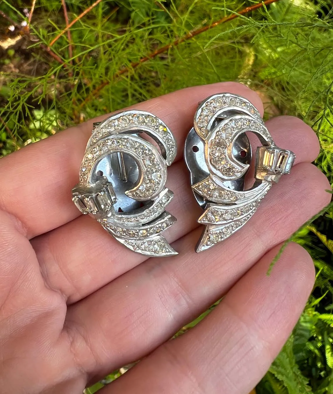 Pair of silver tone and clear paste crystal dress clips styled as curved ribbons.  Green background