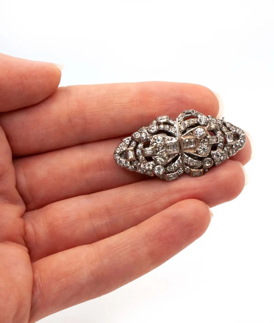 Small double dress clip brooch with clear crystals on silver held in hand