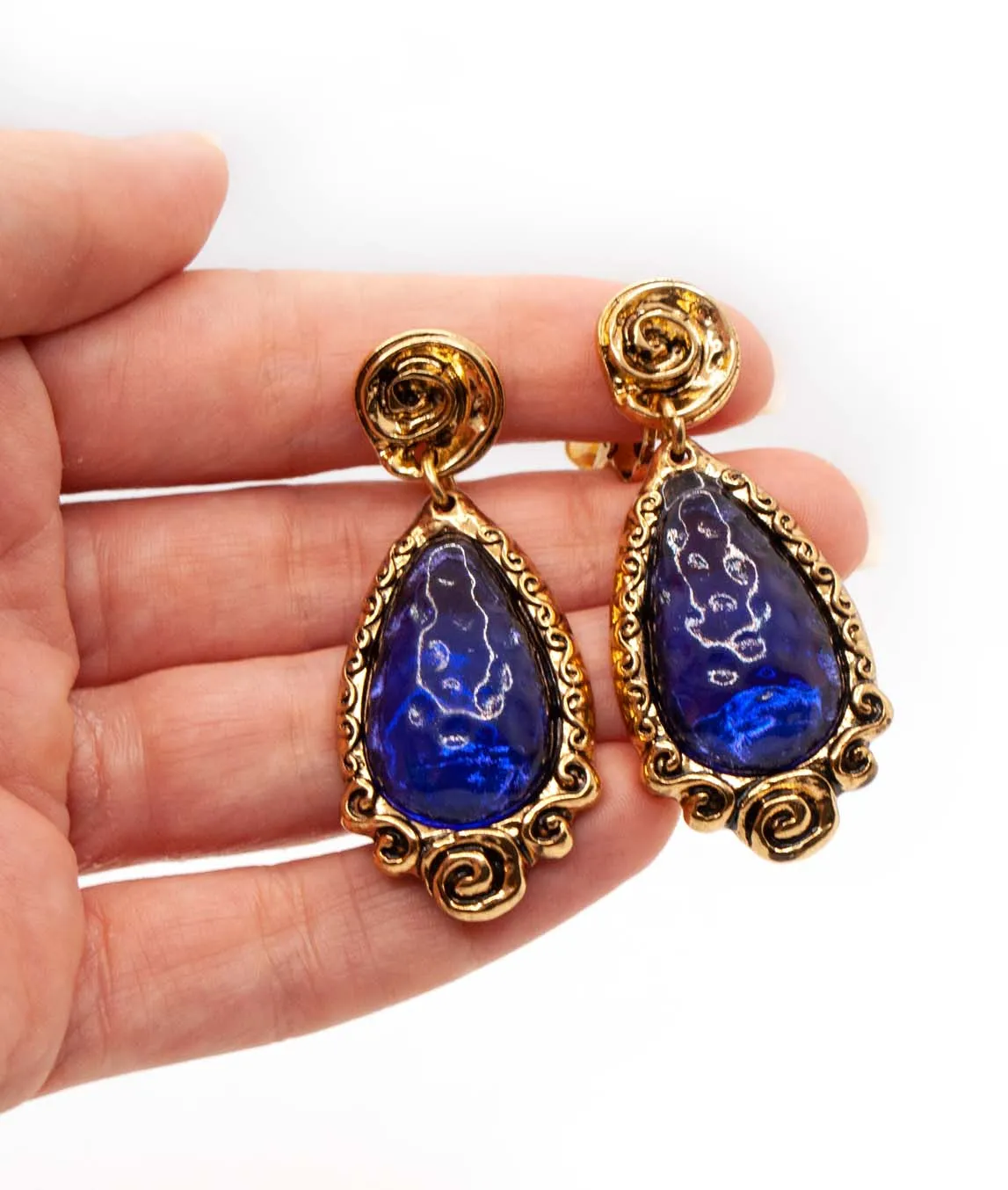 Christian Lacroix Blue Glass Dangle Earrings in a heavy textured gold tone frame held in a hand