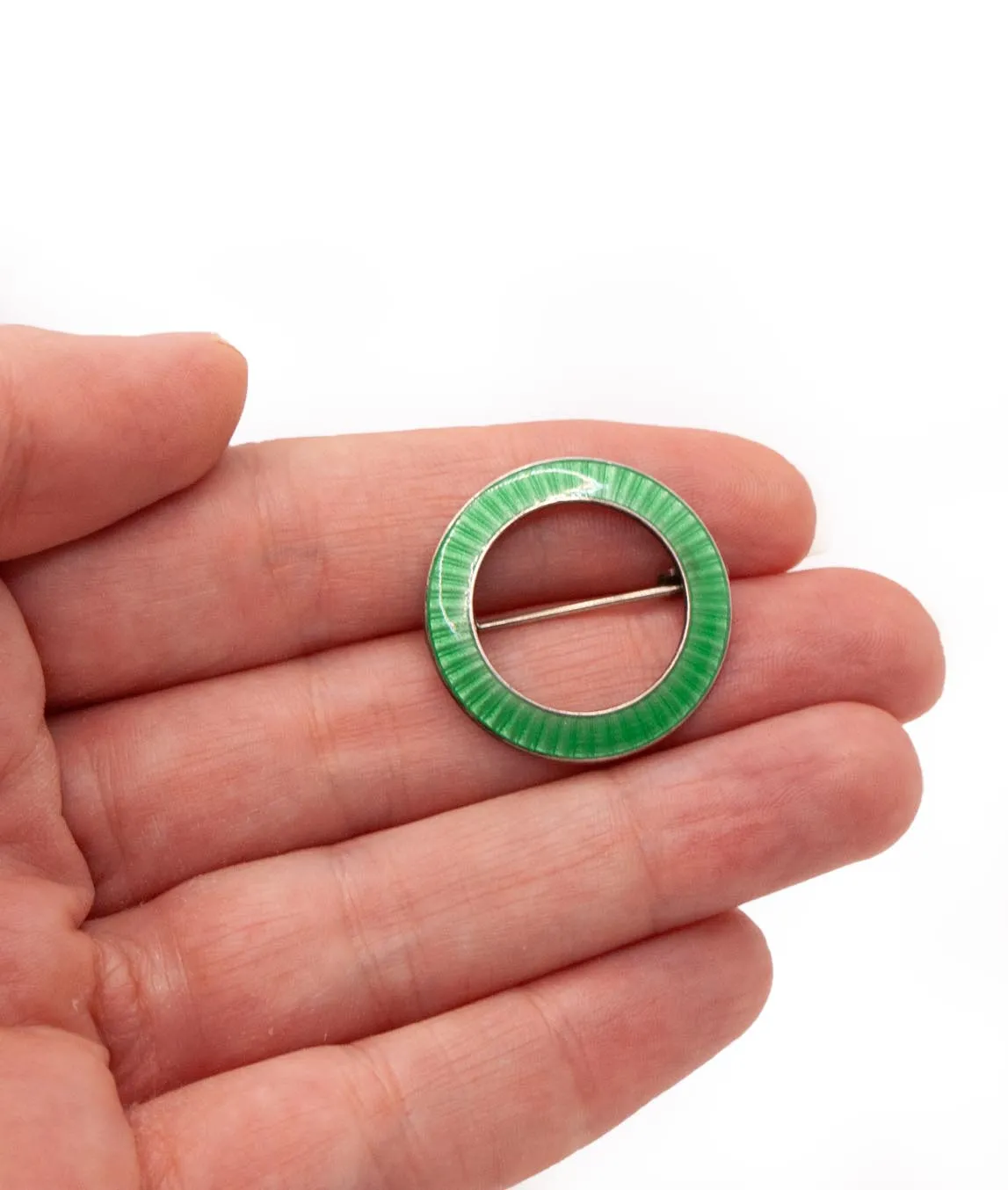 Small circular green enamelled antique brooch held in a hand