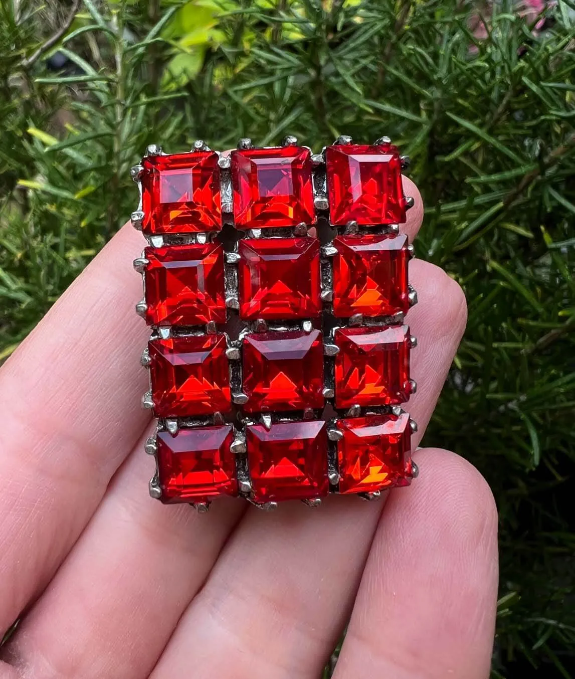 Red rectangular dress clip with square pastes held in a hand photographed outside