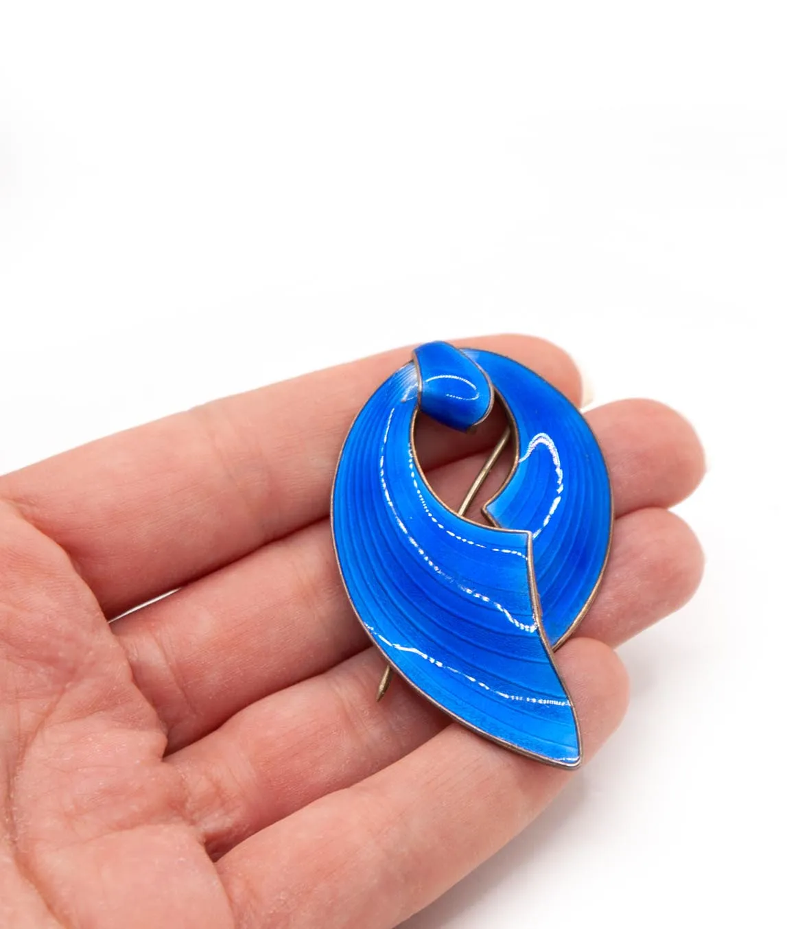 Bright blue enamelled Norwegian ribbon brooch held in a hand