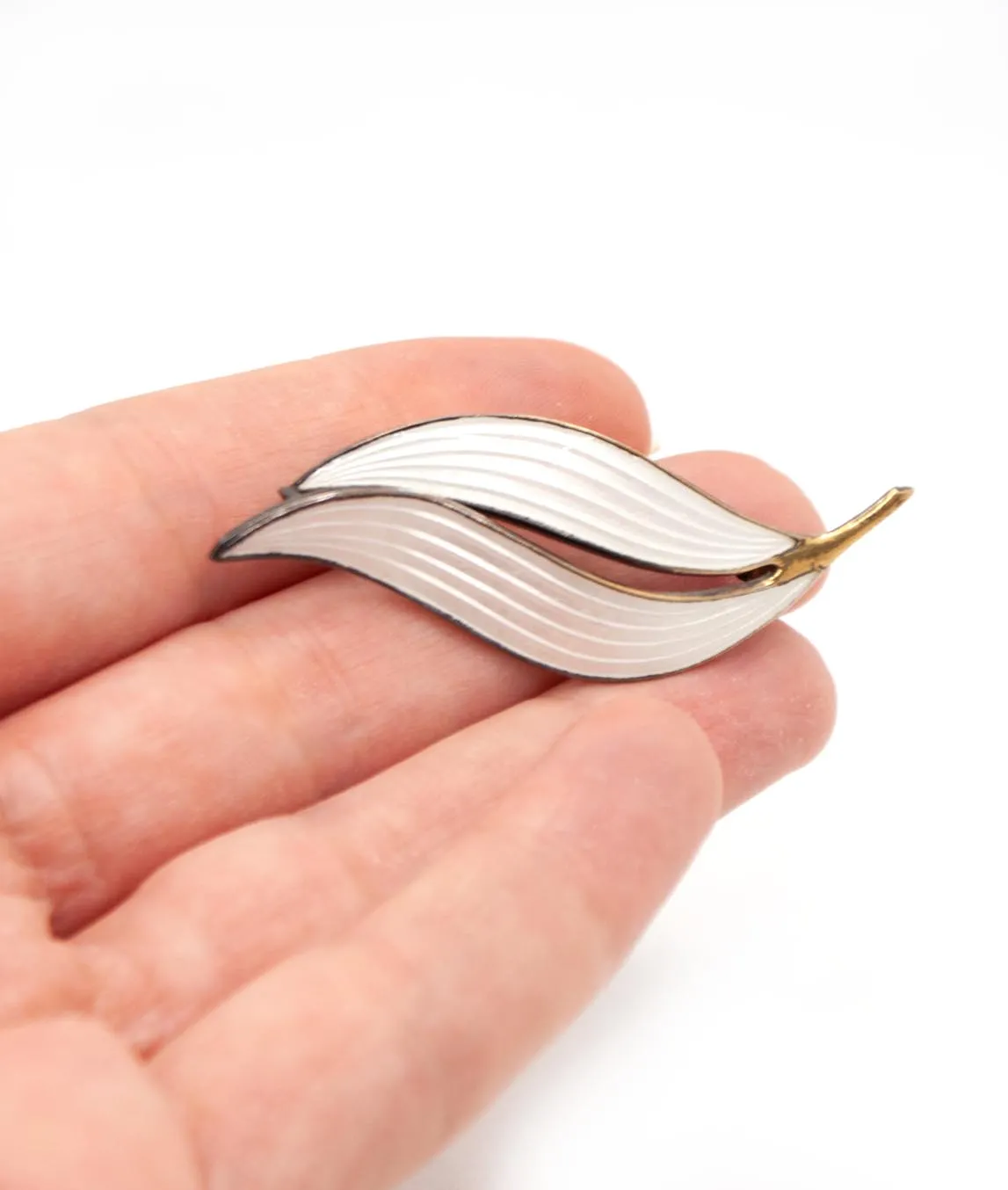 Double leaf white enamel brooch held in hand