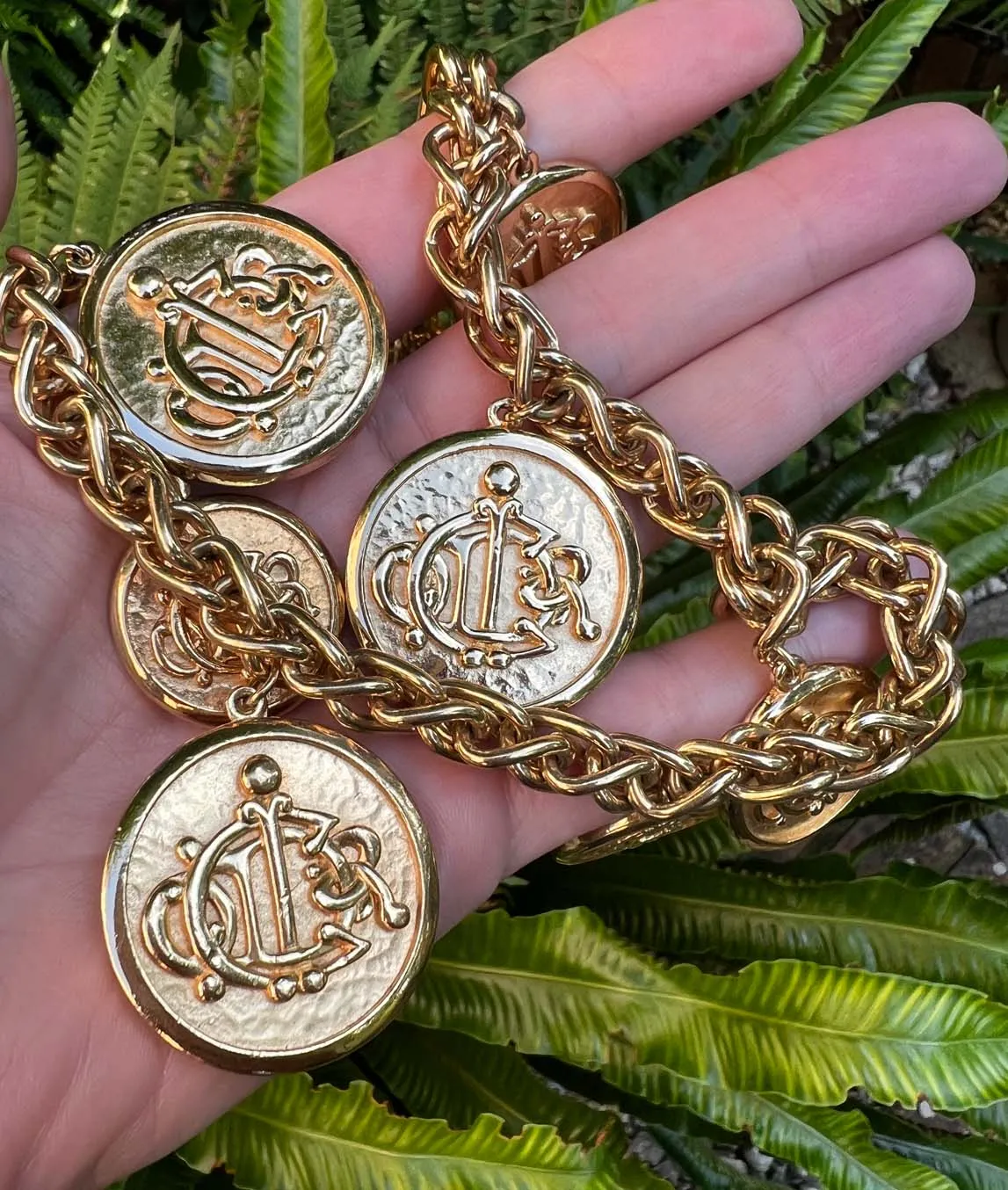 Gold plated heavy link chain with coin charms showing the Christian Dior logo held in a hand with green background
