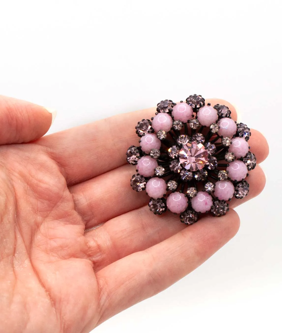 Pink and black vintage round Austrian brooch held in a hand
