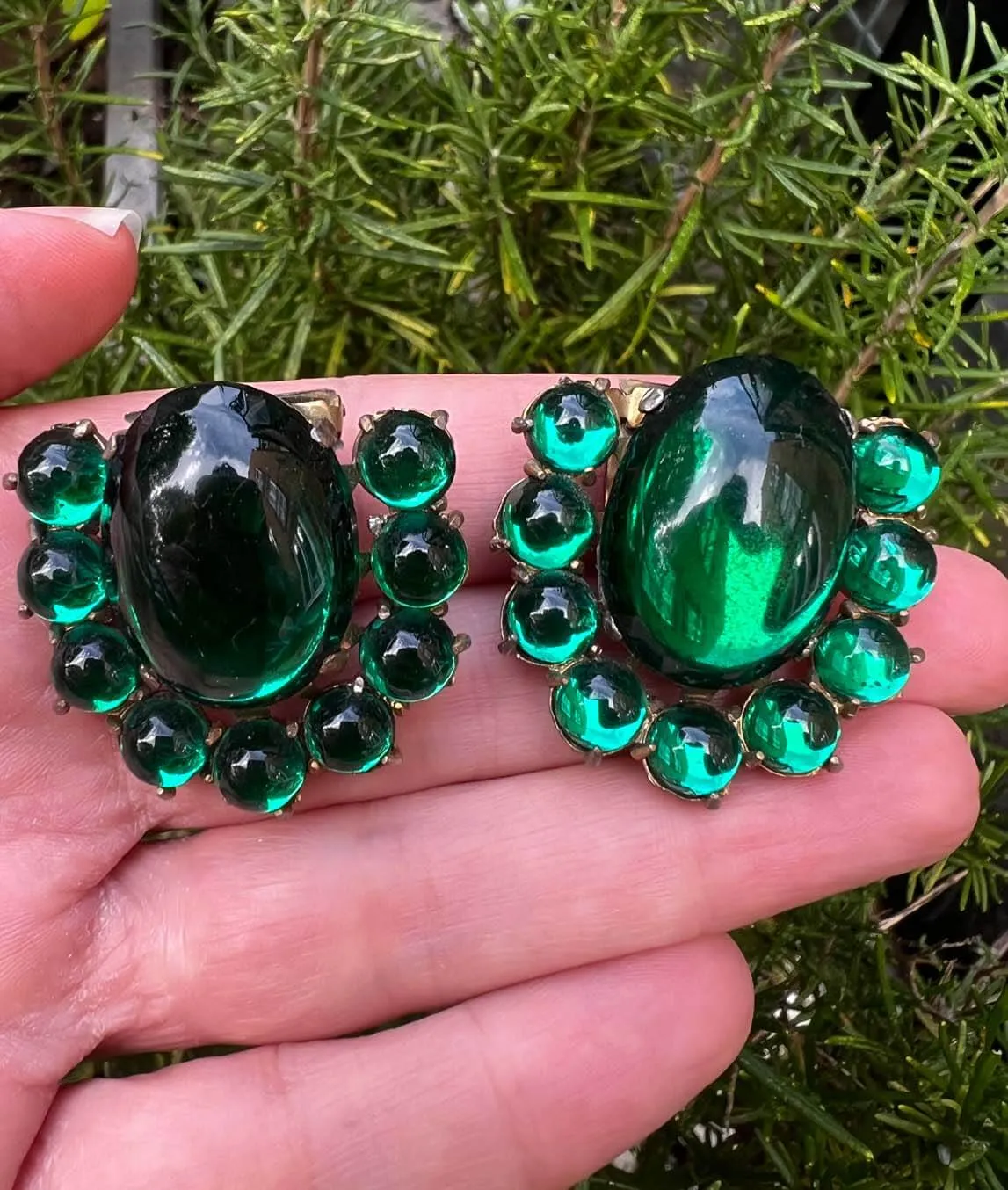Pair of green cabochons dress clips held in a hand with shrubbery background