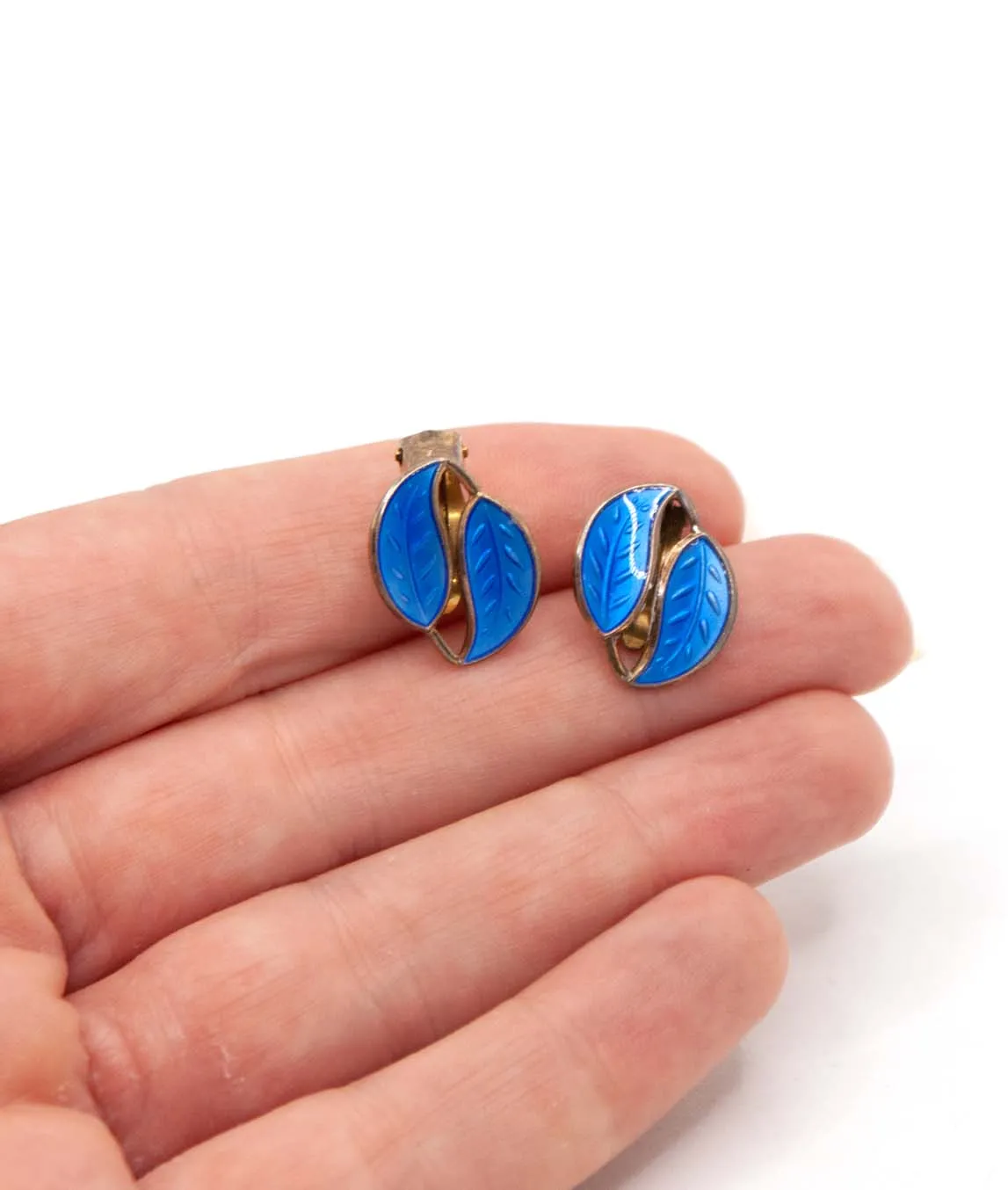 Blue enamel David Andersen leaf earrings held in a hand
